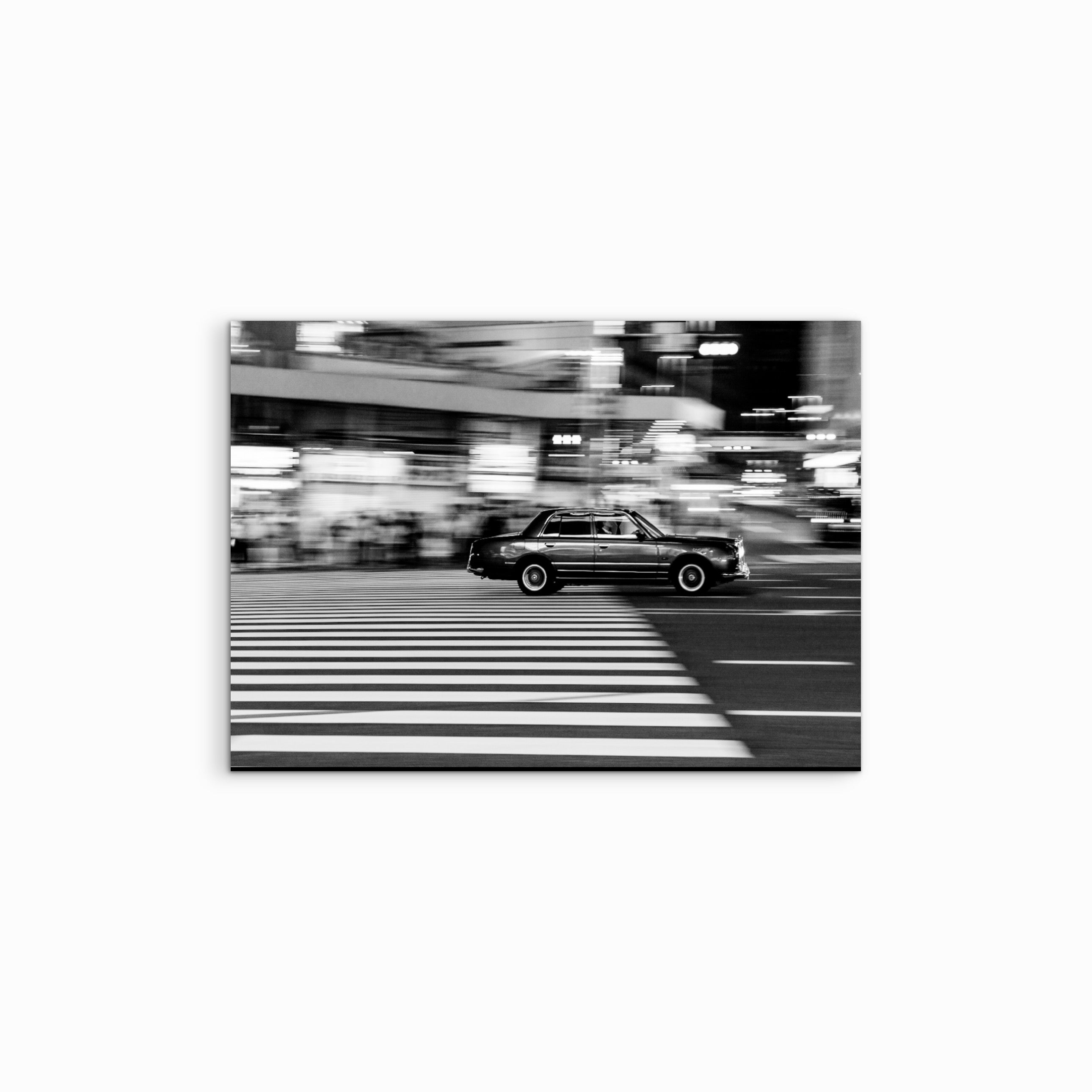 Vor einem weissen Hintergrund präsentiert sich der Fine Art Print „Guilty“, ein dynamisches schwarz-weiss Panning-Shot aus Tokio, das ein vorbeirasendes Taxi verzerrt, aber klar erkennbar zeigt und die urbane Energie der japanischen Metropole einfängt.