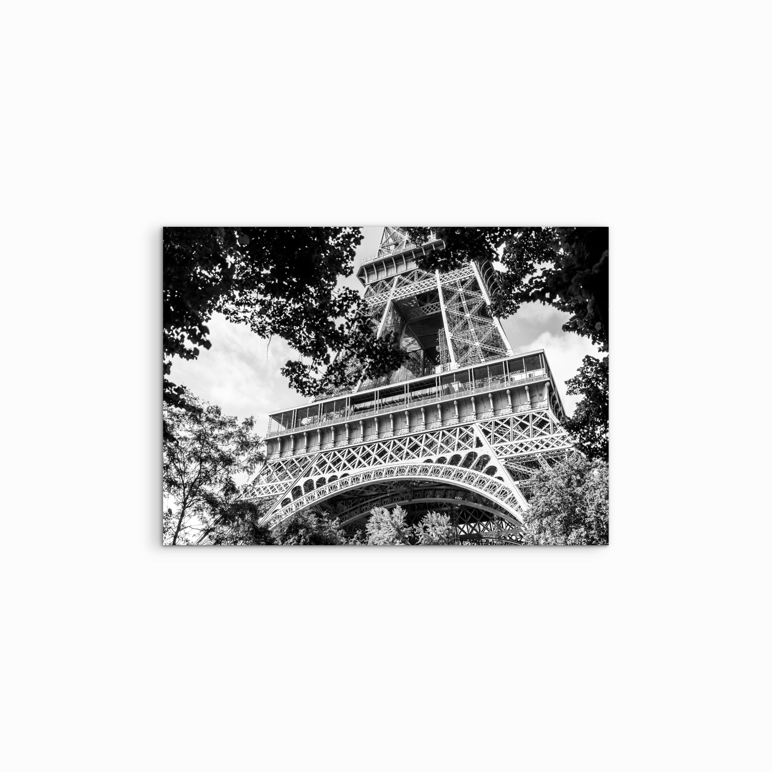 Vor weissem Hintergrund präsentiert sich die Fine Art Fotografie ‚Dissatisfying‘ als schwarz-weiss Aufnahme des unteren Viertels des Eiffelturms, eingerahmt von sommerlichen Bäumen. Der starke Paris-Kontrast, die urbane Architektur und die minimalistische Komposition unterstreichen die klare, zeitlose Bildwirkung.