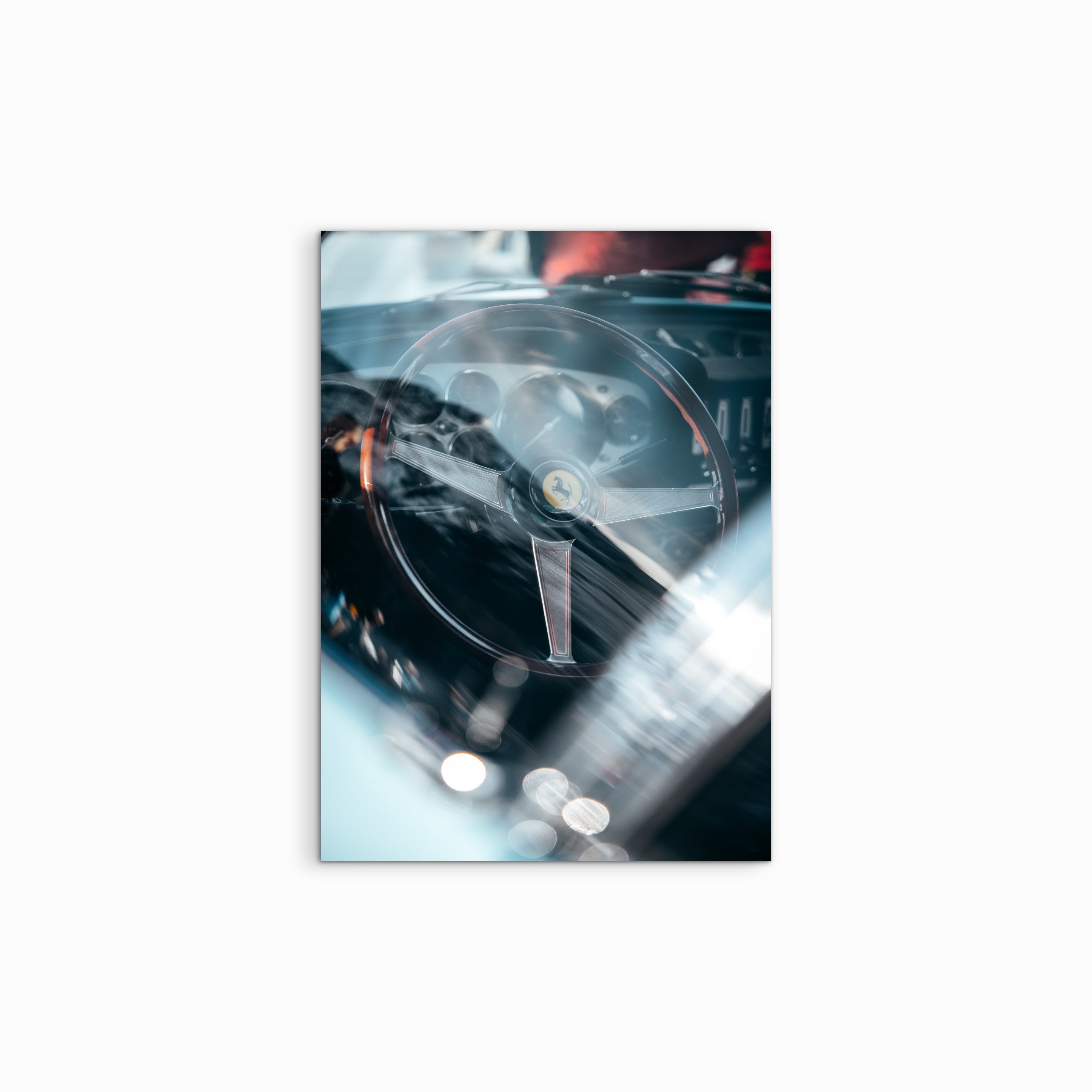 Durch das Seitenfenster eines Vintage-Ferraris zeigt "F. Morning" ein leicht bläulich getöntes Motiv, in dem das hölzerne und metallische Lenkrad mit dem gelben Ferrari-Emblem im Mittelpunkt steht.